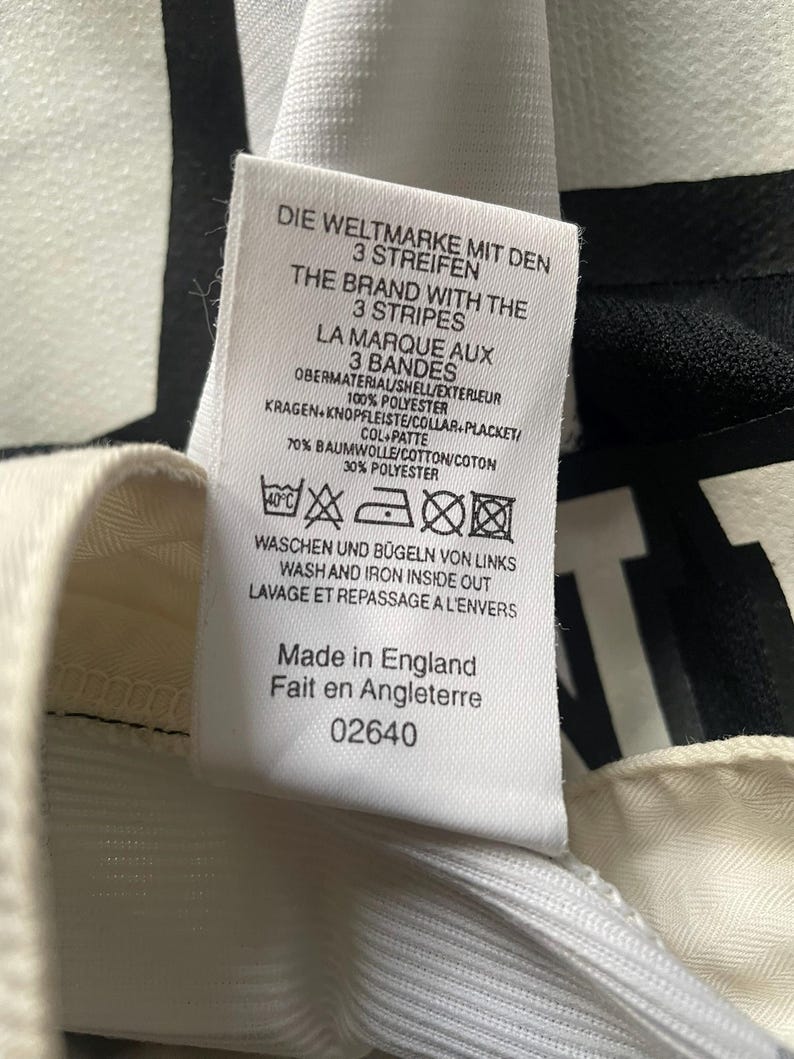 May include: Close-up of a white tag with text in multiple languages, including English, German, and French. The tag lists fabric composition as 70% cotton and 30% polyester. The text also includes washing instructions and the phrase "Made in England."