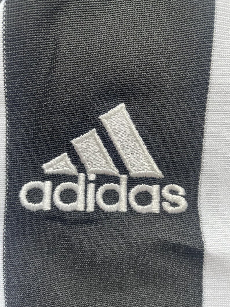 May include: A white adidas logo with three stripes embroidered on a black fabric background.