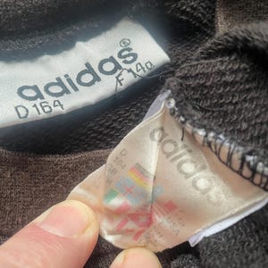 May include: A close-up of a brown Adidas sweatshirt tag with the text "adidas" and "D 164 F 140".