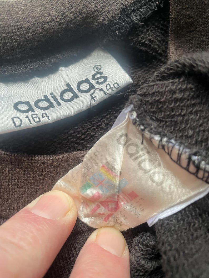 May include: A close-up of a brown Adidas sweatshirt tag with the text "adidas" and "D 164 F 140".