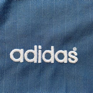 May include: A close-up of a blue fabric with the word "adidas" embroidered in white.
