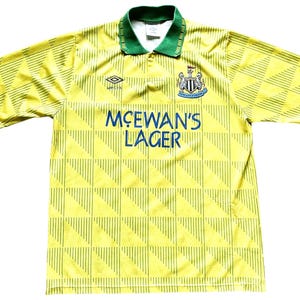 May include: A yellow and green soccer jersey with a black and white team logo and the text "McEWAN'S LAGER" on the front.