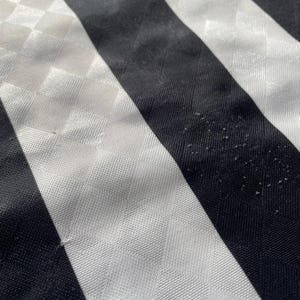 Op de afbeelding: Close-up van een vintage Newcastle United voetbalshirt. Het shirt heeft zwart-witte verticale strepen, met een ruitpatroon op de witte strepen. Het teamembleem is zichtbaar bovenaan, met "Newcastle United" op een blauwe banner.