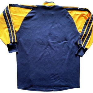 May include: A long-sleeved shirt with a navy blue body and yellow sleeves. The sleeves have three yellow stripes on each side.