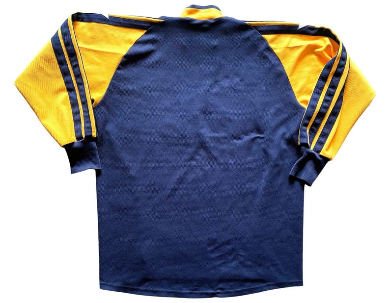 May include: A long-sleeved shirt with a navy blue body and yellow sleeves. The sleeves have three yellow stripes on each side.