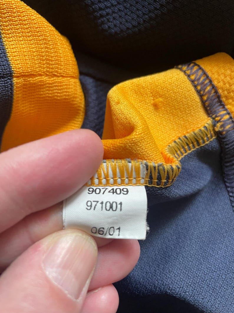 May include: Close-up of a white tag with black text. The tag reads "907409 971001 06/01".