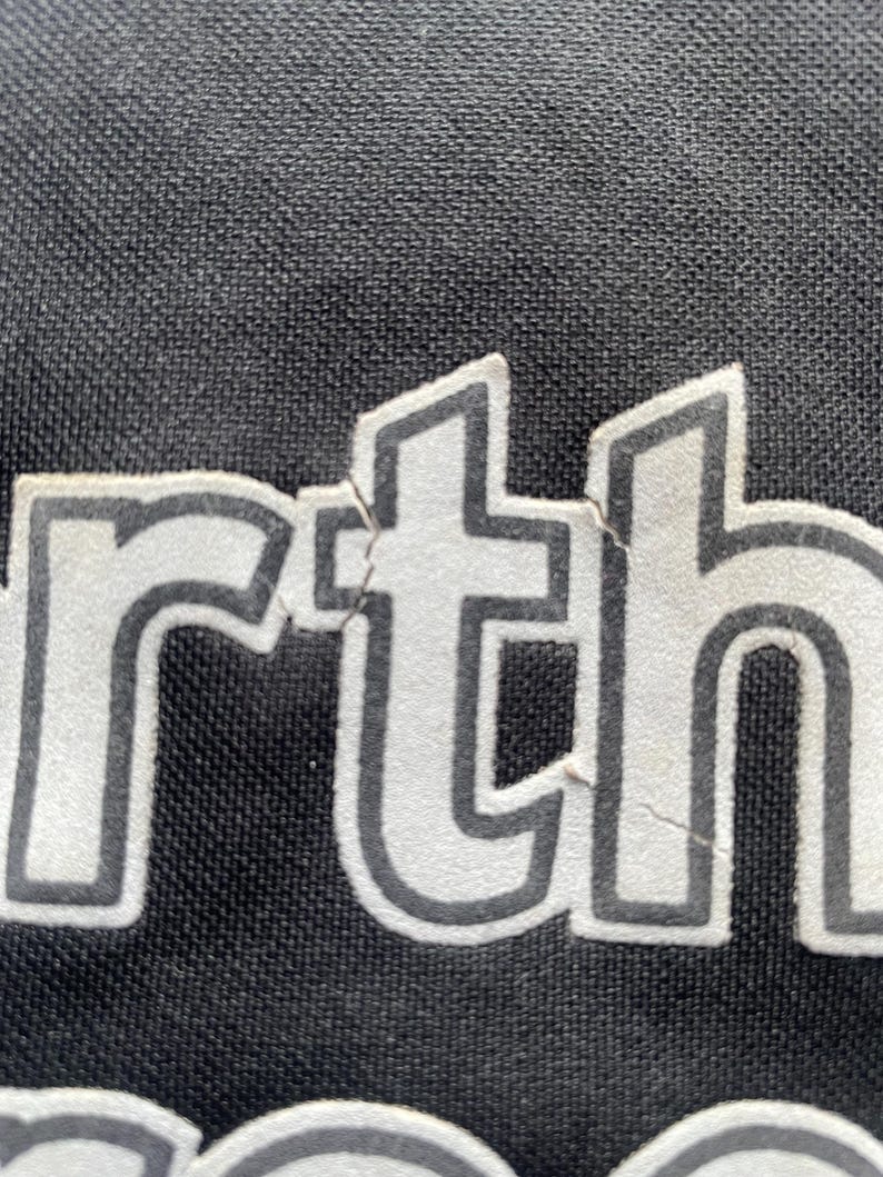 以下が含まれることがあります： 黒い衣服のクローズアップで、白い文字で「rth」と印刷されています。
