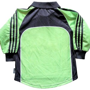 May include: A long-sleeved soccer jersey with black and white stripes on the sleeves. The jersey is green with a black collar and a white trim around the collar. The jersey has a white logo on the front.