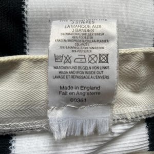 May include: Close-up of a white and black striped fabric with a tag attached. The tag includes text in English, French, and German, with washing instructions and the phrase "Made in England". The fabric is likely part of a garment.