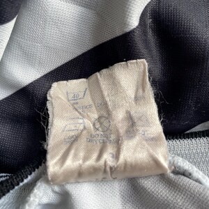 May include: A white tag with black text and symbols. The tag has instructions for washing and drying the garment. The text includes "Machine Wash", "Do Not Bleach", "Tumble Dry Low", and "Iron Low".