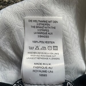 May include: White tag with black text that reads "Die Weltmarke mit den 3 Streifen", "The Brand with the 3 Stripes", "La Marque aux 3 Bandes", "100% Polyester", "Waschen und B&uuml;geln von Links", "Wash and Iron Inside Out", "Lavage et Repassage a l'Envers", "Made in U.K.", "Fabrique au Royaume-Uni", "16593". The tag also has a 40 degree Celsius washing symbol, a do not bleach symbol, a tumble dry low symbol, and an iron low symbol.