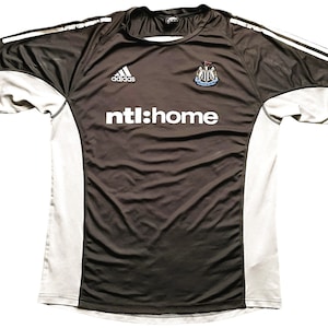 May include: Black and gray soccer jersey with white accents. The jersey has the Adidas logo, the Newcastle United crest, and the text "ntl:home" on the front.