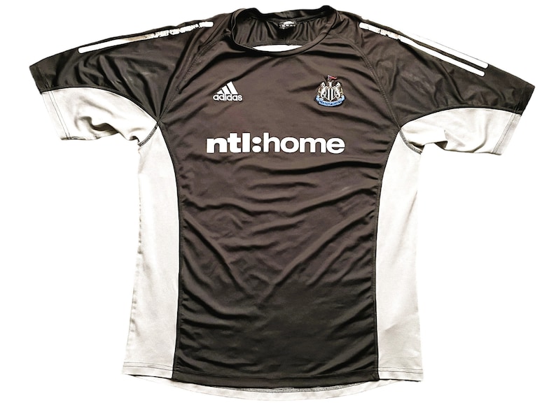 May include: Black and gray soccer jersey with white accents. The jersey has the Adidas logo, the Newcastle United crest, and the text "ntl:home" on the front.