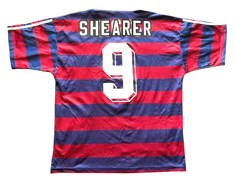 May include: A red and blue striped jersey with the name "SHEARER" and the number "9" in white. The jersey has white stripes on the sleeves.