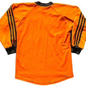 May include: Orange long-sleeved shirt with black stripes on the sleeves.