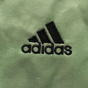 May include: A close-up of a green Adidas logo with black stitching. The logo is embroidered on a green fabric.