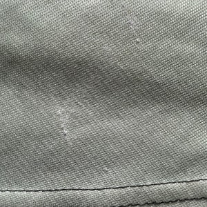 May include: Close-up of olive green fabric with a textured surface. The fabric has a visible seam at the bottom and some minor imperfections.