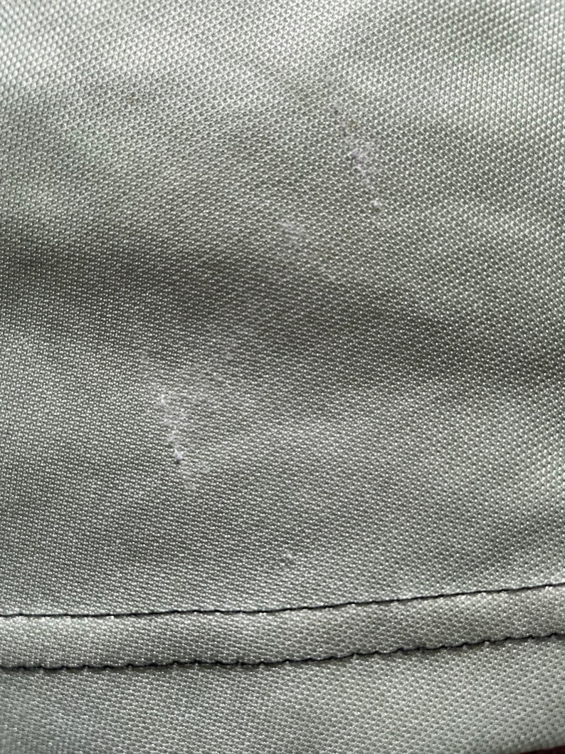 May include: Close-up of olive green fabric with a textured surface. The fabric has a visible seam at the bottom and some minor imperfections.