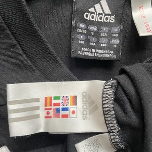 May include: Black Adidas t-shirt with a white Adidas logo and size tag. The tag shows sizes in UK, USA, EU, and J, and the text "Made in Indonesia, Fabriqu&eacute; en Indon&eacute;sie".