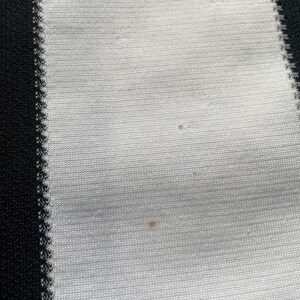 May include: Close-up of a white and black striped fabric. The fabric has a ribbed texture with vertical stripes. The black stripes are on the left and right edges, with white stripes in between. There are a few small spots on the white fabric.