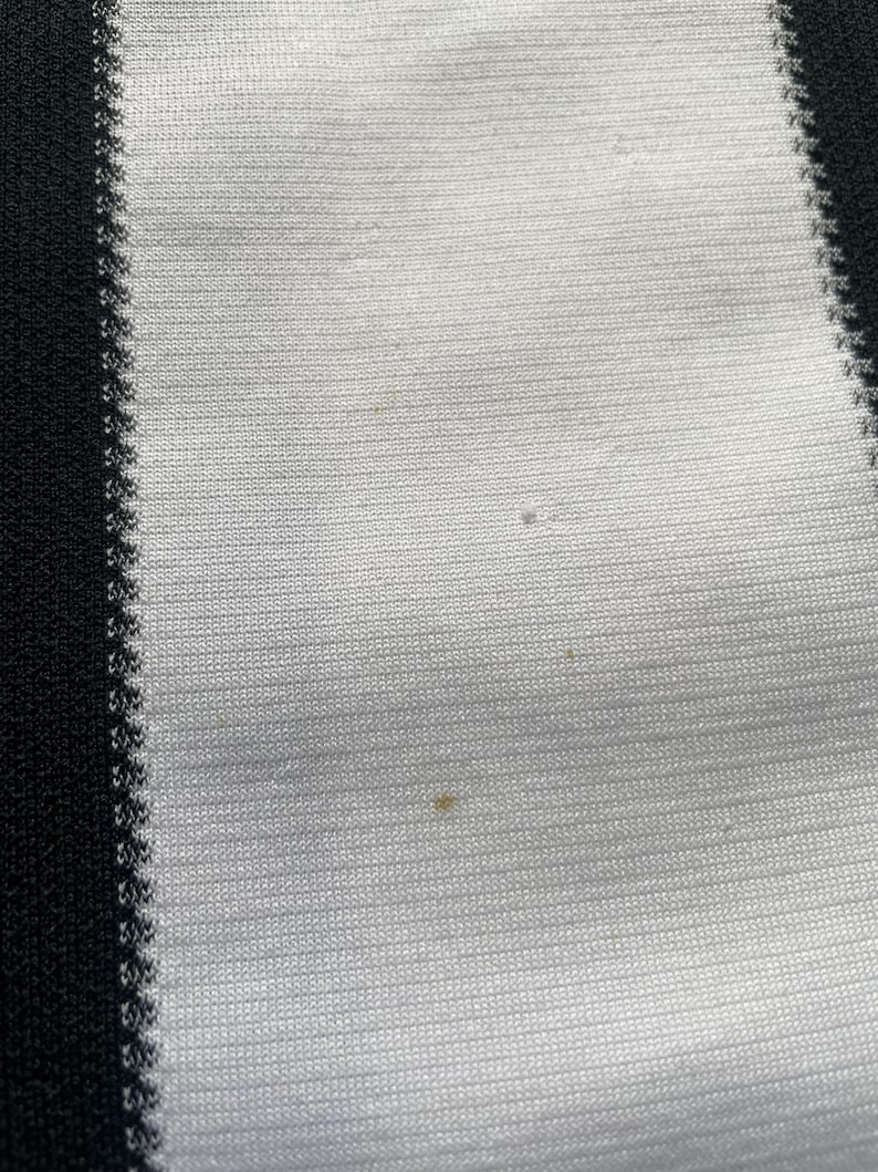 May include: Close-up of a white and black striped fabric. The fabric has a ribbed texture with vertical stripes. The black stripes are on the left and right edges, with white stripes in between. There are a few small spots on the white fabric.