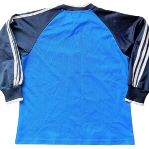 May include: A blue long-sleeved shirt with black and white striped sleeves. The shirt has a crew neck and is made of a soft, comfortable material.