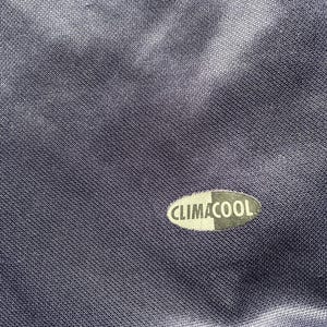 May include: Close-up of a navy blue athletic garment with the text "CLIMACOOL" in white and black. The fabric has a subtle sheen and a textured weave, suggesting a performance material.