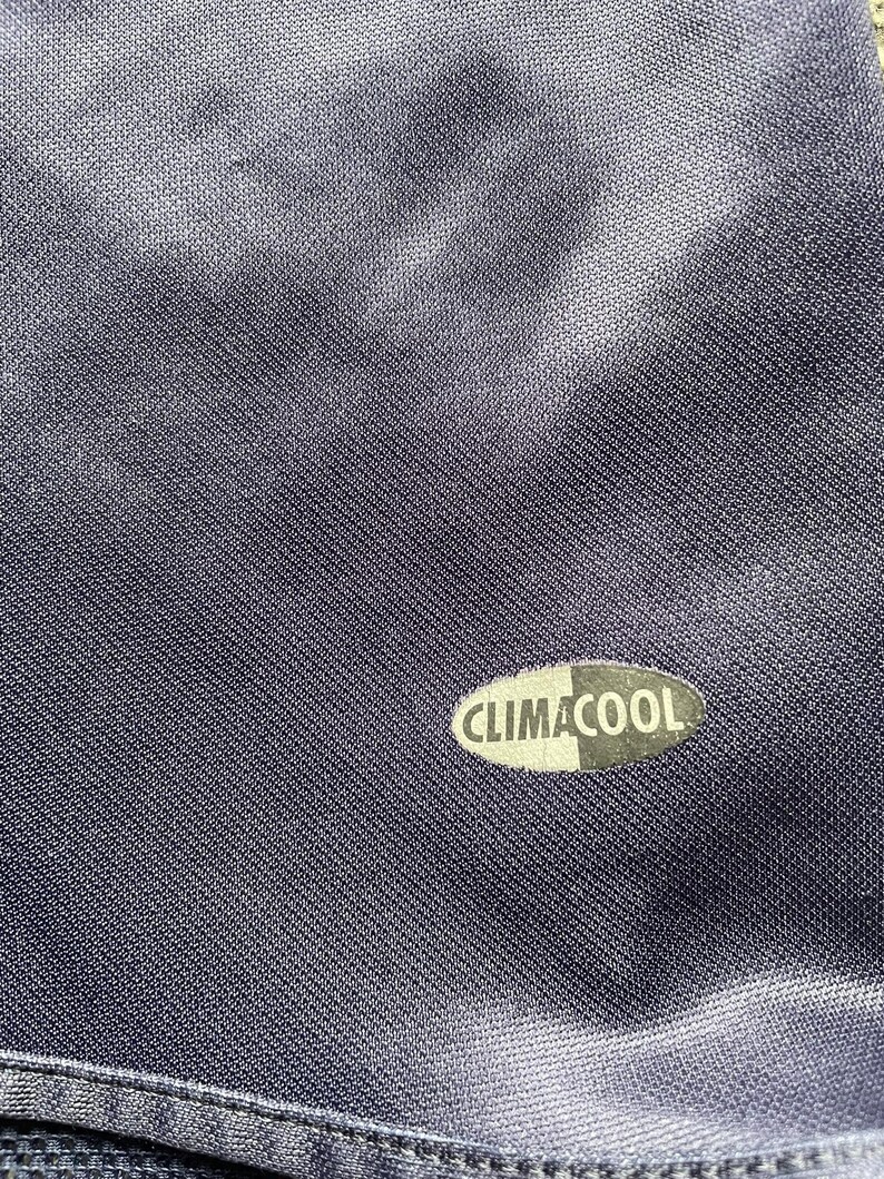 May include: Close-up of a navy blue athletic garment with the text "CLIMACOOL" in white and black. The fabric has a subtle sheen and a textured weave, suggesting a performance material.