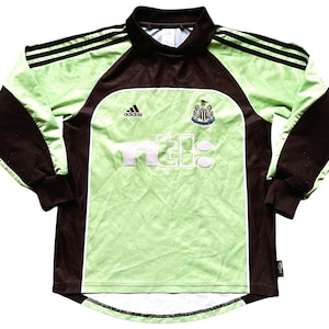 May include: A green and brown long-sleeved soccer jersey with the Adidas logo, the Newcastle United crest, and the text "n.e.b.c." on the front.