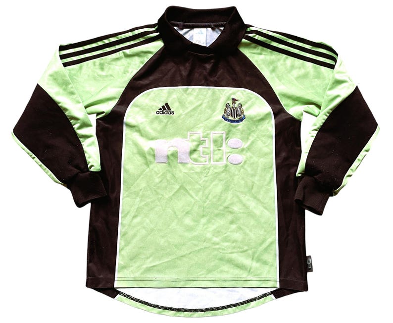 May include: A green and brown long-sleeved soccer jersey with the Adidas logo, the Newcastle United crest, and the text "n.e.b.c." on the front.