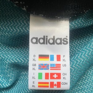 May include: A white tag with the word "adidas" in black text. The tag shows size conversions for different countries, including Germany, France, Great Britain, the United States, Italy, Switzerland, Spain, and Canada.