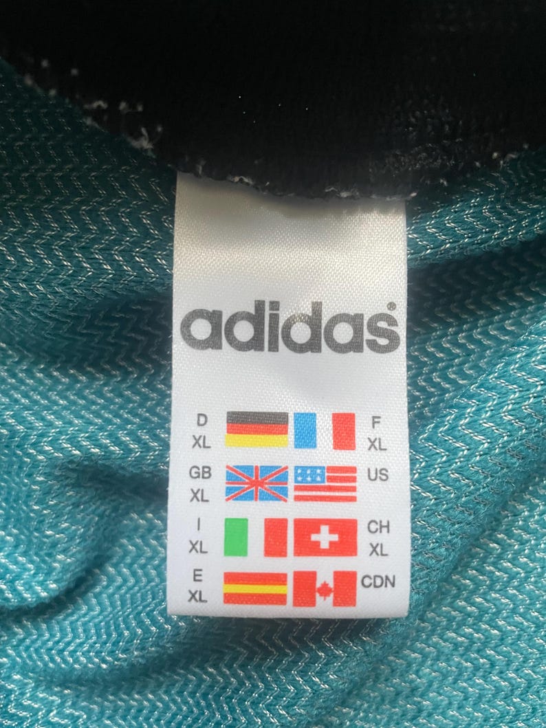 May include: A white tag with the word "adidas" in black text. The tag shows size conversions for different countries, including Germany, France, Great Britain, the United States, Italy, Switzerland, Spain, and Canada.