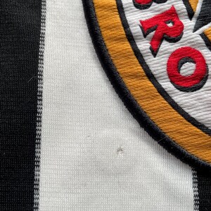 Puede incluir: Camiseta de f&uacute;tbol a rayas blancas y negras con un parche bordado amarillo, negro y rojo que dice "BRO" en rojo.