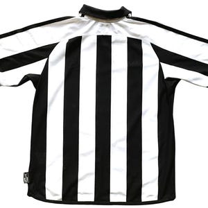 Pode incluir: Camisola de futebol de riscas pretas e brancas com uma guarni&ccedil;&atilde;o azul em volta do colarinho e das mangas.