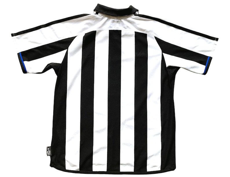 Pode incluir: Camisola de futebol de riscas pretas e brancas com uma guarni&ccedil;&atilde;o azul em volta do colarinho e das mangas.