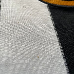 Może przedstawiać: Zbliżenie na biało-czarną tkaninę w paski z małą, haftowaną naszywką z napisem "Wigan" czerwonymi literami.