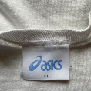 May include: White t-shirt with a blue "asics" label and "LB" written below the logo.