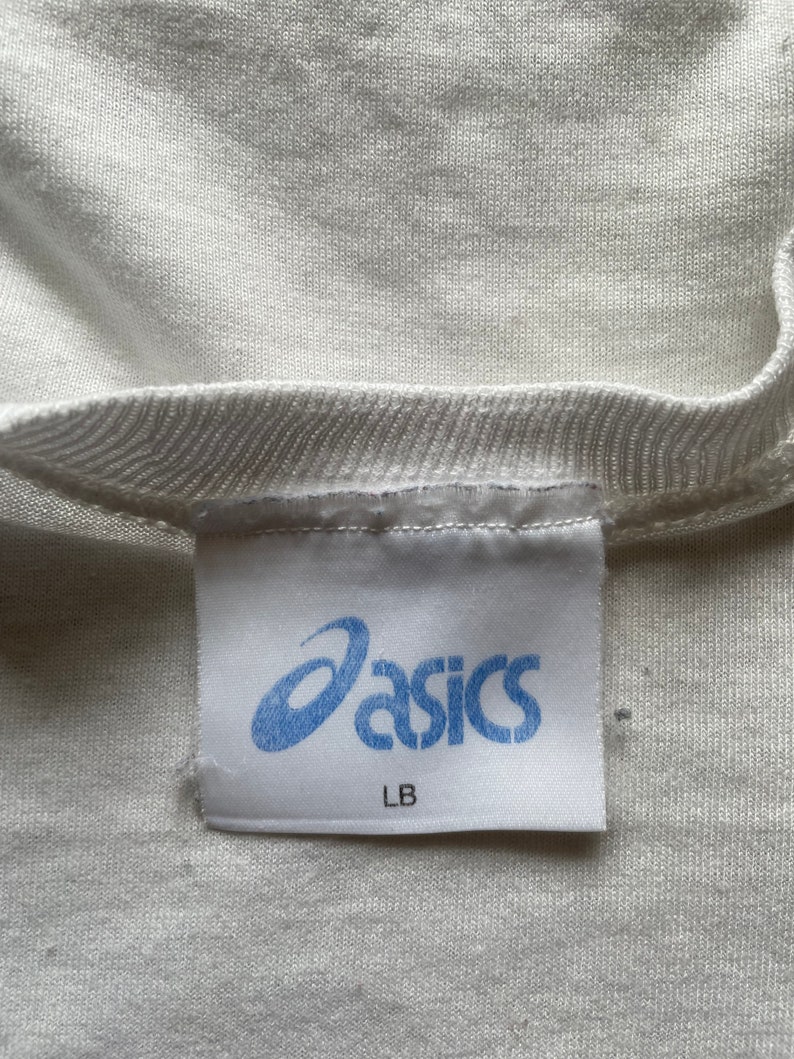 May include: White t-shirt with a blue "asics" label and "LB" written below the logo.