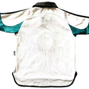Pu&ograve; includere: Maglia da calcio a maniche corte bianca con dettagli neri e turchesi. La maglia ha un colletto nero e una striscia nera su ogni manica.