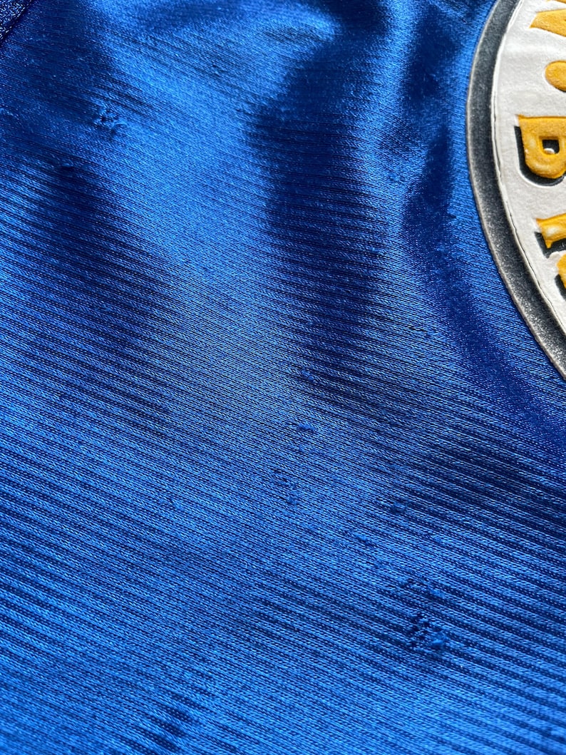 K&ouml;nnte beinhalten: Nahaufnahme eines blauen Stoffes mit einem strukturierten Muster. Der Stoff hat mehrere kleine L&ouml;cher.