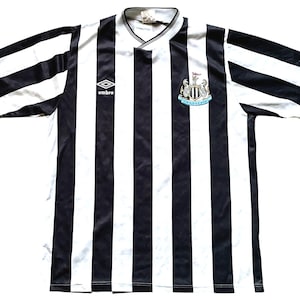 May include: Black and white striped soccer jersey with the Newcastle United crest and the Umbro logo.