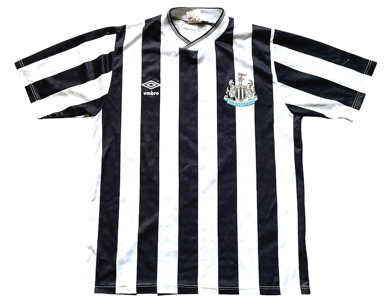 May include: Black and white striped soccer jersey with the Newcastle United crest and the Umbro logo.