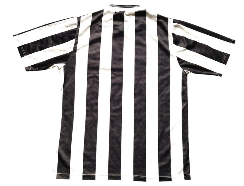 May include: Black and white striped soccer jersey. The jersey has a classic design with a crew neck and short sleeves.