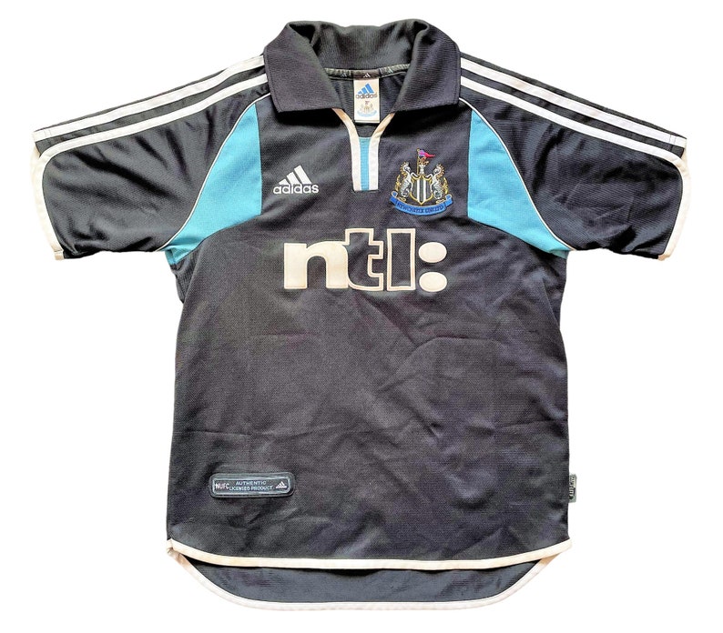 Op de afbeelding: Een zwart voetbaltenue met witte en blauwe accenten. Het tenue heeft het Adidas-logo, het Newcastle United-wapen en het NTL-logo. Het tenue is gemaakt van een lichtgewicht, ademende stof.