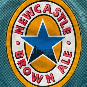 Pu&ograve; includere: Una maglia color teal con il logo Newcastle Brown Ale. Il logo ovale presenta uno sfondo giallo, una stella blu e la scritta "NEWCASTLE BROWN ALE" in rosso. La maglia ha un motivo strutturato.