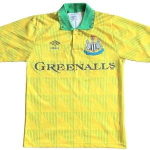 K&ouml;nnte beinhalten: Ein gelbes und gr&uuml;nes Fu&szlig;balltrikot mit einem schwarz-wei&szlig;en Teamwappen und dem Schriftzug "Greenalls" auf der Vorderseite. Das Trikot hat einen gr&uuml;nen Kragen und ein wei&szlig;es Logo auf der rechten Brustseite.