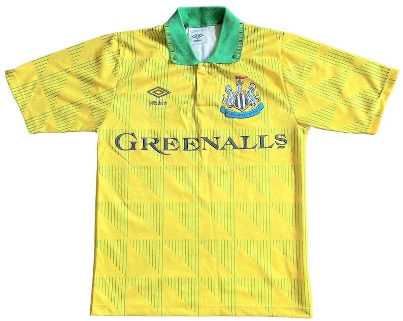 K&ouml;nnte beinhalten: Ein gelbes und gr&uuml;nes Fu&szlig;balltrikot mit einem schwarz-wei&szlig;en Teamwappen und dem Schriftzug "Greenalls" auf der Vorderseite. Das Trikot hat einen gr&uuml;nen Kragen und ein wei&szlig;es Logo auf der rechten Brustseite.