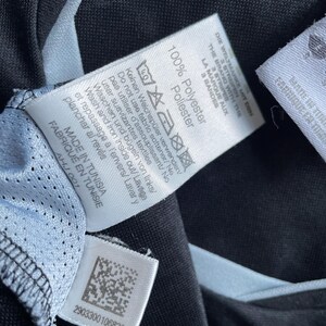 May include: A black and white care label with the text "100% Polyester" and instructions for washing and ironing the garment. The label also includes the text "Made in Tunisia" and a barcode.