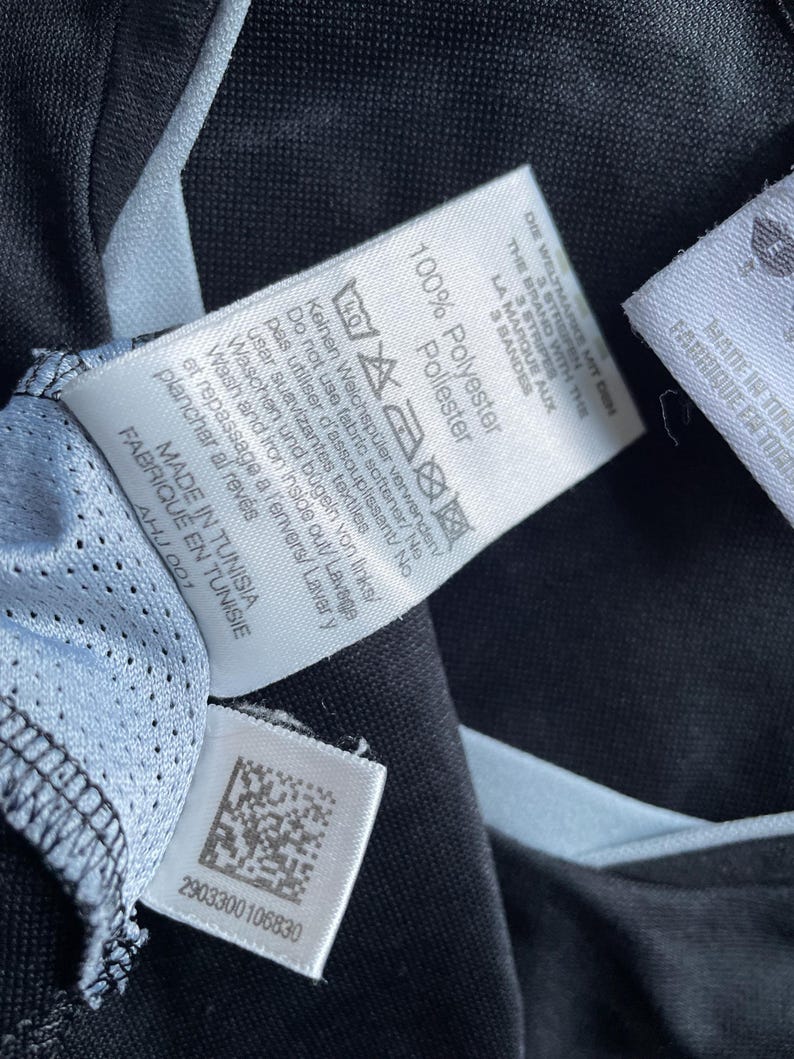 May include: A black and white care label with the text "100% Polyester" and instructions for washing and ironing the garment. The label also includes the text "Made in Tunisia" and a barcode.