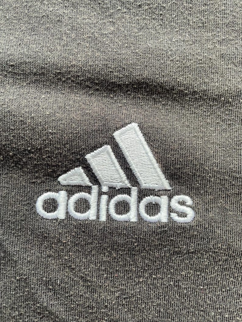 May include: A close-up of a gray t-shirt with a white embroidered Adidas logo.